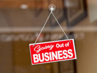 Red sign hanging at the glass door of a shop saying: "Going out of business".