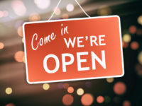 We are open sign hanging on a glass storefront